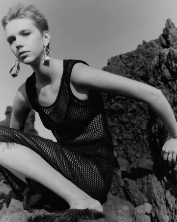 Monochrome portrait of a short-haired woman in a black mesh dress posing against dark rocky terrain by Nicolas Kern.