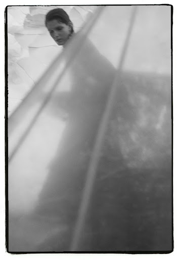 Monochrome portrait of a woman partially obscured by translucent layered fabric with a dark frame border