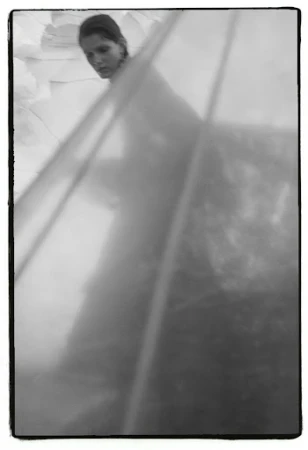 Monochrome portrait of a woman partially obscured by translucent layered fabric with a dark frame border