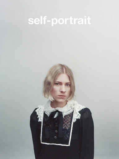 Blonde woman in a vintage black dress with lace collar, posing against a light grey background. Close-up studio portrait with bright light.