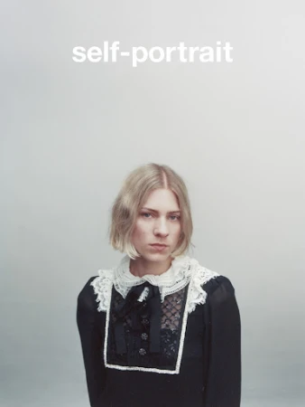 Blonde woman in a vintage black dress with lace collar, posing against a light grey background. Close-up studio portrait with bright light.