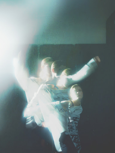Blured motion of a person in a light-filled indoor space, wearing a long-sleeved shirt against a dark background, creating a sense of movement.