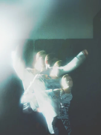 Blured motion of a person in a light-filled indoor space, wearing a long-sleeved shirt against a dark background, creating a sense of movement.