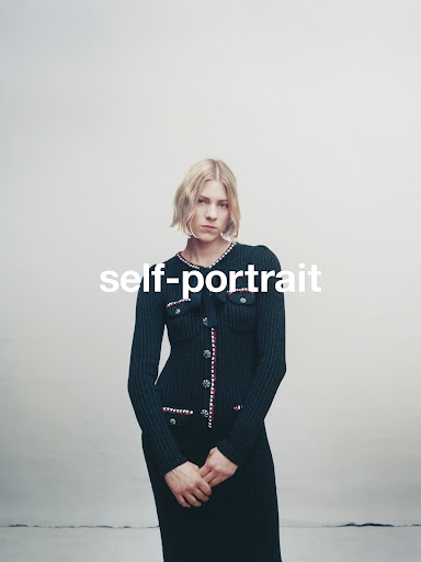 Woman in a navy blue knit dress posing in a studio, facing forward. The dress has white and red trim and pearl details.