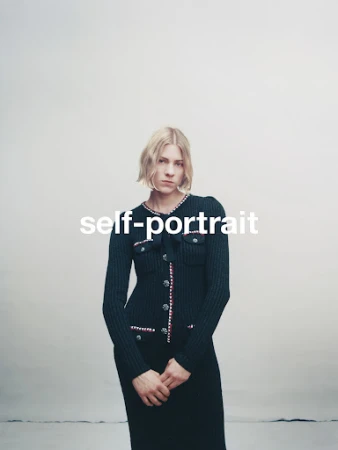 Model with blonde bob hair wearing a black knitted cardigan with white and red trim against a neutral studio background