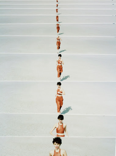 Woman in orange sportswear running against white floor, captured in a repetitive sequence, showing her progression across the frame.