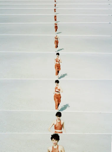 Woman in orange sportswear running against white floor, captured in a repetitive sequence, showing her progression across the frame.