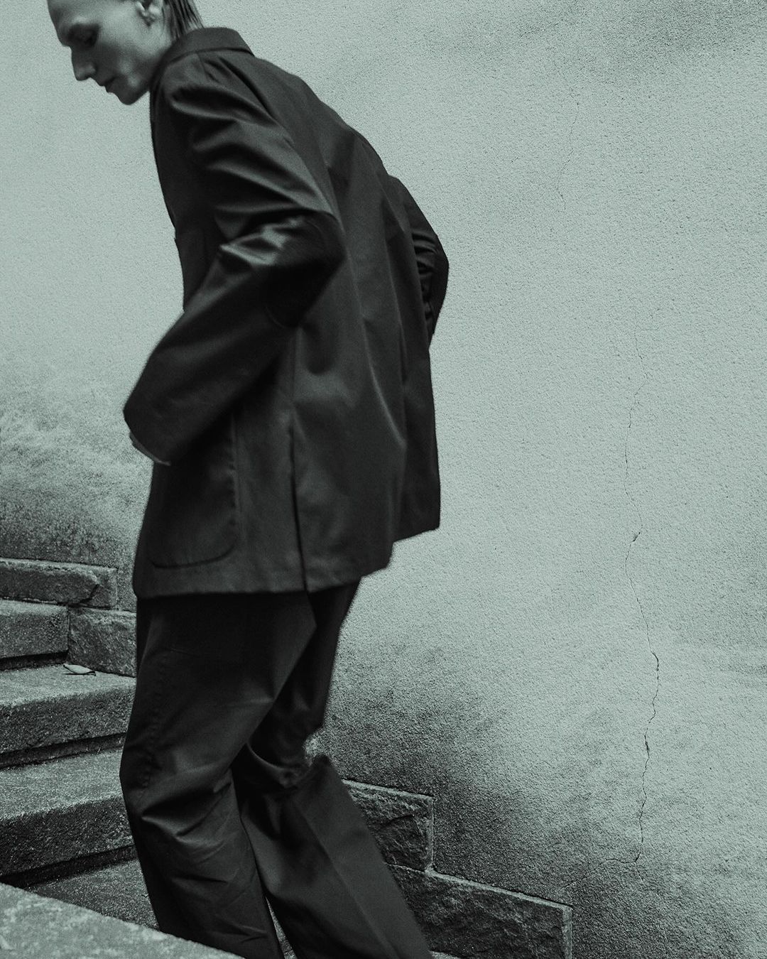 Adult male in a suit walking down stone steps outdoors. The photo features desaturated teal tones and high contrast.