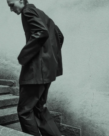 Adult male in a suit walking down stone steps outdoors. The photo features desaturated teal tones and high contrast.