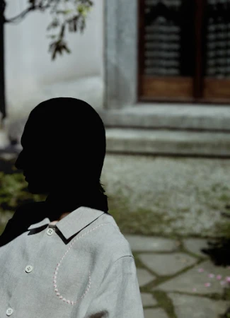 Silhouette of a person wearing a light grey buttoned jacket with decorative stitching outdoors