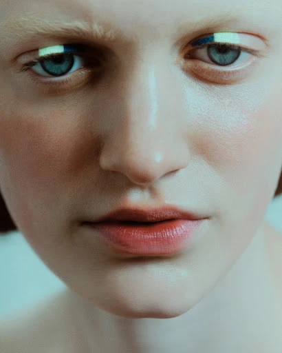 Close-up portrait of a fair-skinned person with striking blue and green eyeliner, focusing on facial details and makeup artistry.
