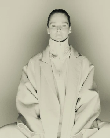 Monochrome portrait of a model wearing a high-collared knit sweater and oversized coat against a neutral background
