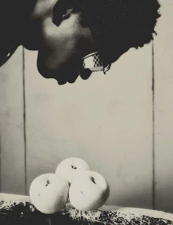 Monochrome portrait of a black man wearing checkered sunglasses looking down at three white round objects