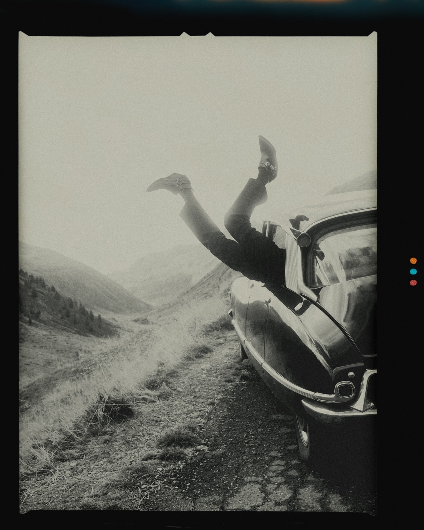 Person's legs sticking out of a vintage car window in a mountainous landscape, creating a sense of freedom and adventure.