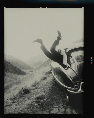 Person's legs sticking out of a vintage car window in a mountainous landscape, creating a sense of freedom and adventure.