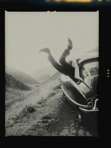 Person hanging upside down out of a vintage car window on a mountain road captured by Nicolas Kern