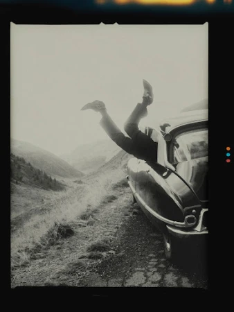 Person hanging upside down out of a vintage car window on a mountain road captured by Nicolas Kern