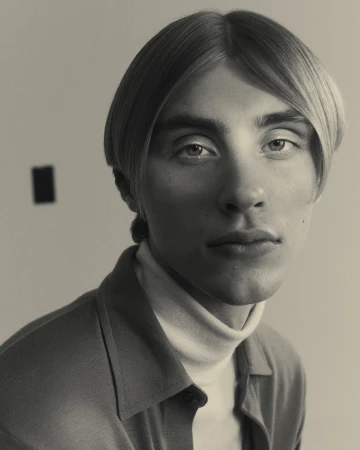 Portrait of a man with blonde hair and a white turtleneck photographed by Nicolas Kern against a plain wall.