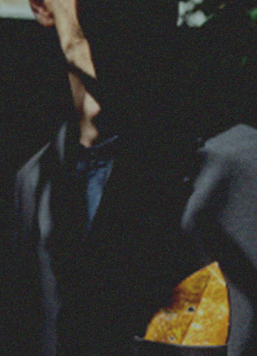 Close-up of an adult wearing a dark suit, dress shirt, and pocket square. The man's face is obscured by shadow.