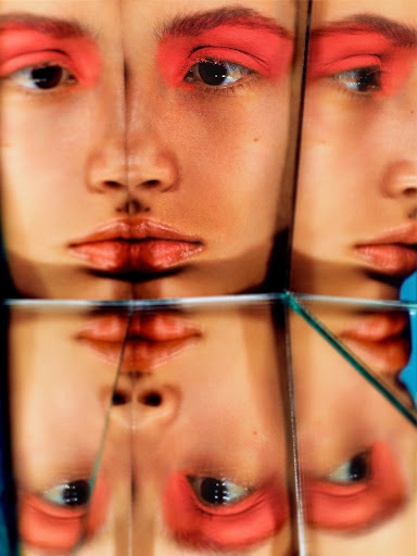 Close-up studio portrait of an adult female face with a red eyeshadow makeup effect, fragmented into geometric mirrored glass tiles.