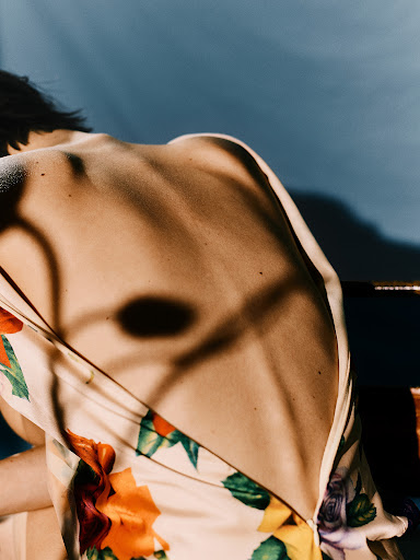 Close-up of a person's bare back wearing a floral patterned dress against a blue backdrop with dramatic shadows
