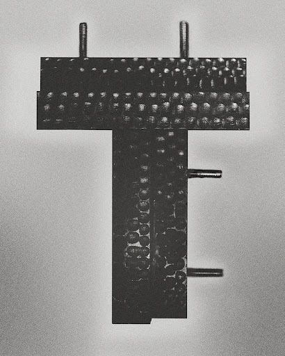 Close-up of a black metal T-shaped industrial component with bolts against a gradient gray background in a studio setting.