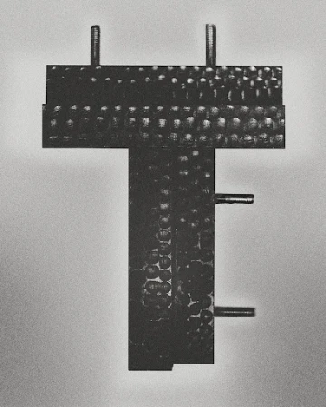 Close-up of a black metal T-shaped industrial component with bolts against a gradient gray background in a studio setting.