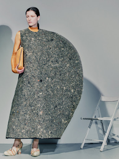 Model in architectural grey felt dress and orange top holding a clutch, photographed by Nicolas Kern against a grey background