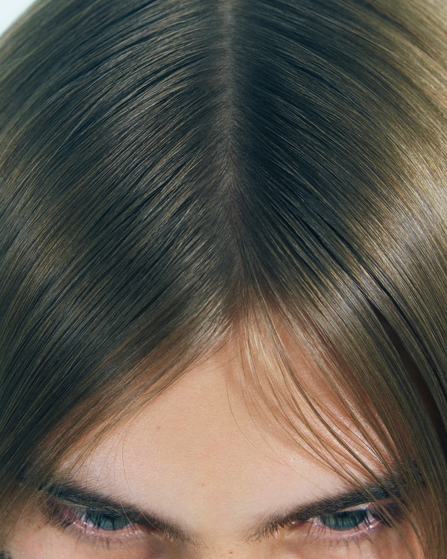 Close-up portrait of a person with straight brown hair parted down the middle, showing eyes and forehead.