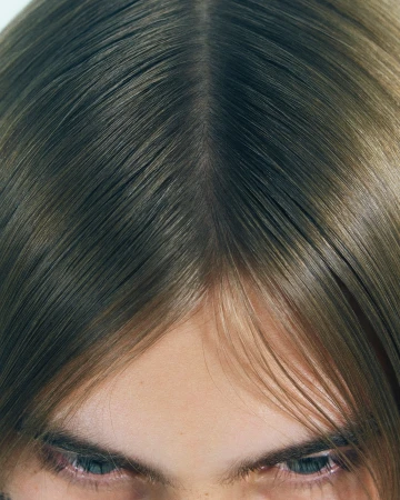 Close-up portrait of a person with straight brown hair parted down the middle, showing eyes and forehead.