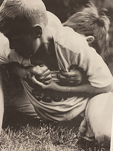 Black and white image of two boys wrestling on grass, one in a light-colored t-shirt with a graphic, outdoors during daytime.