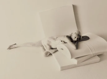 Model lying across stacked white foam blocks wearing a pale textured dress and pointed-toe heels
