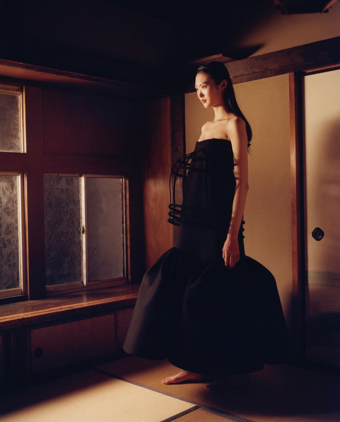 A slender Asian woman models a strapless black gown in a room with Japanese shoji doors and windows for a fashion editorial.