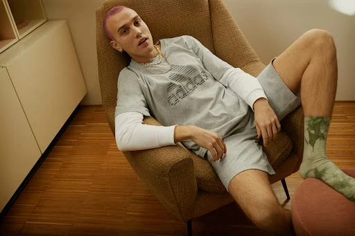 Man with pink hair wearing grey adidas t shirt seated in an armchair