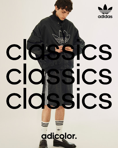 Adidas fashion shoot features a male model in a black jacket and shorts with striped socks and loafers against a white background.