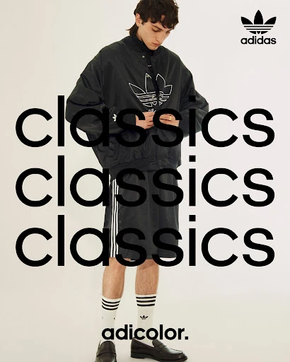 Adidas fashion shoot features a male model in a black jacket and shorts with striped socks and loafers against a white background.
