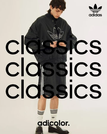 Adidas fashion shoot features a male model in a black jacket and shorts with striped socks and loafers against a white background.