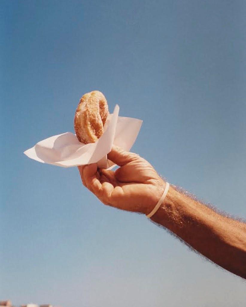 A hand holding a churro with a paper napkin against a clear blue sky, providing a simple, bright, and appetizing image.