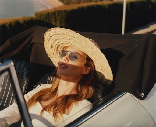 Woman in a wide-brimmed straw hat and sunglasses sitting in a classic convertible car shot by Paolo Zerbini