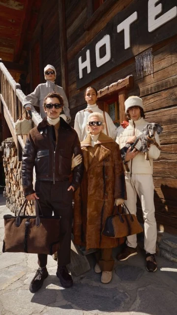 Group portrait of five people with a small dog in front of a wooden building. People are wearing winter clothing and carrying bags.