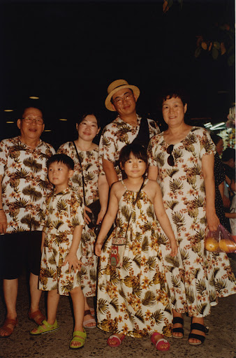Group portrait of a family of six wearing matching floral print outfits, including two children, posing outdoors in a softly lit area.