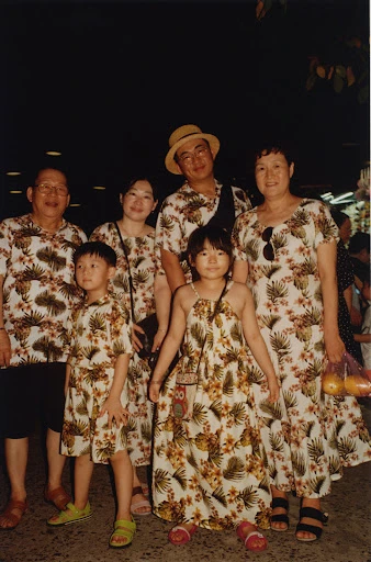 Group portrait of a family of six wearing matching floral print outfits, including two children, posing outdoors in a softly lit area.