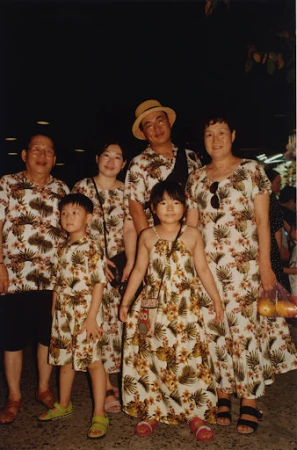 Group portrait of a family of six wearing matching floral print outfits, including two children, posing outdoors in a softly lit area.
