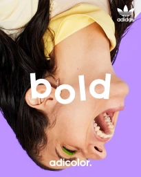 Close-up inverted portrait of a person with dark hair, open mouth, and bright green eye makeup against a solid purple background.
