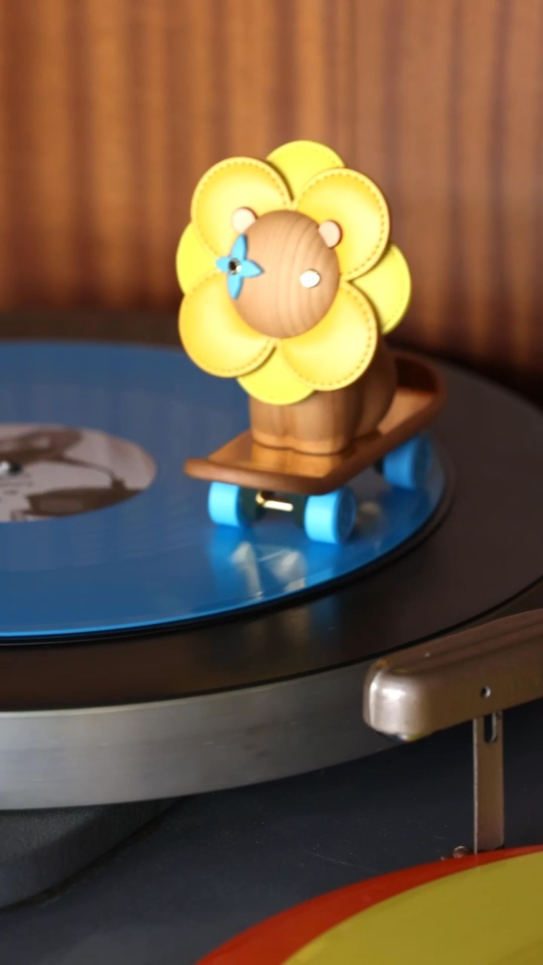 Toy lion on a skateboard positioned on a record player, close-up shot with a wooden background. Child's toy and music.