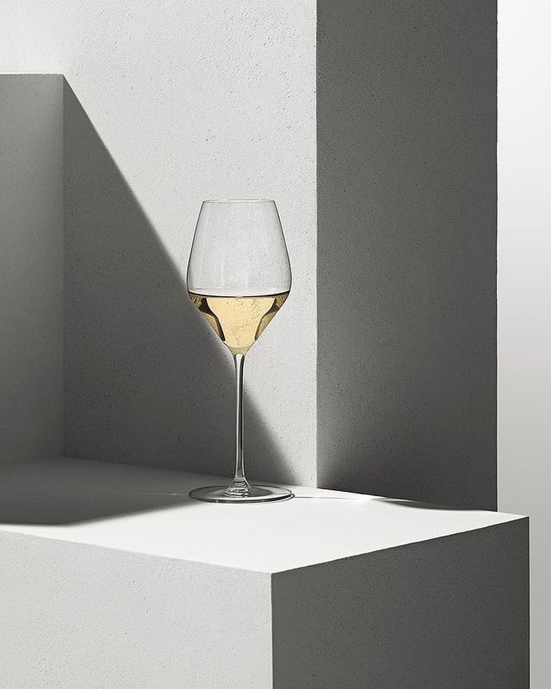 Elegant champagne flute filled with sparkling wine on a geometric concrete pedestal with sharp shadows and neutral tones, still life.