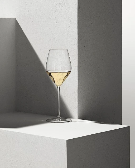 Elegant champagne flute filled with sparkling wine on a geometric concrete pedestal with sharp shadows and neutral tones, still life.