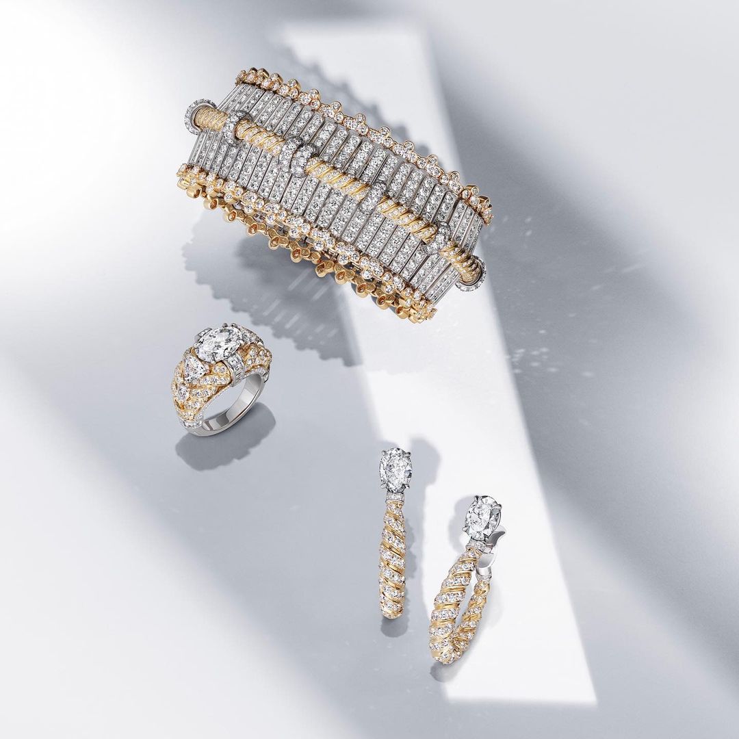 A bracelet, ring, and two earrings sit on a gray surface with a beam of light across them, showcasing the jewelry and diamonds.