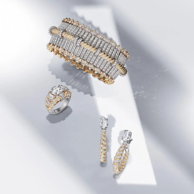 A bracelet, ring, and two earrings sit on a gray surface with a beam of light across them, showcasing the jewelry and diamonds.