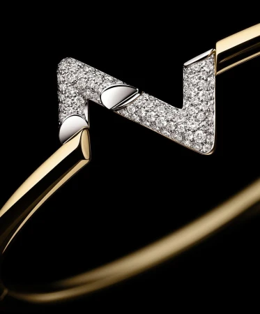 Close-up of a gold and diamond pavé geometric bangle bracelet against a dark background